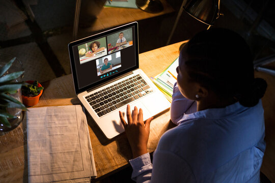 African american woman using laptop for video call, with diverse elementary school pupils on screen