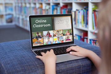 Caucasian girl using laptop for video call, with smiling diverse elementary school pupils on screen