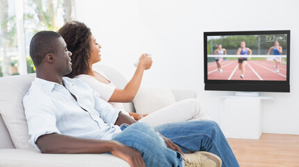 Rear view of african american couple sitting at home together watching athletics event on tv