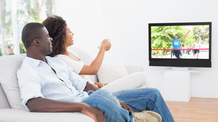 Rear view of african american couple sitting at home together watching athletics event on tv