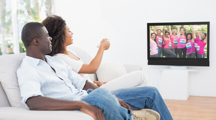 Rear view of african american couple sitting at home together watching athletics event on tv