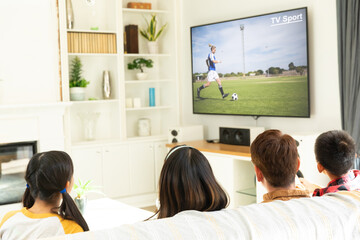 Rear view of family sitting at home together watching football match on tv