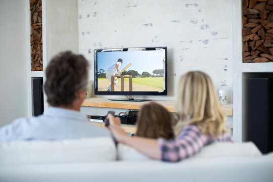 Rear View Of Family Sitting At Home Together Watching Cricket Match On Tv