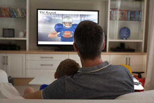 Rear View Of Father And Son Sitting At Home Together Watching Sport Event On Tv