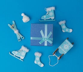 Top view of a gift box and accessories for winter sports and recreation on a blue background.