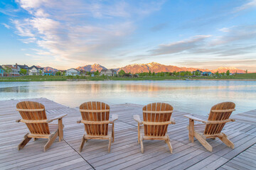 Four wooden lounge chairs facing the reflective Oquirrh Lake at Daybreak, Utah