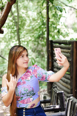 Fototapeta premium Mujer joven tomándose una fotografía con el teléfono o haciendo una videollamada. Mujer Guatemalteca en un ambiente natural.