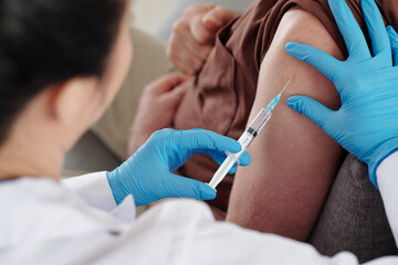 Medical nurse in protective gloves injecting vaccine against coronavirus in shoulder of patient