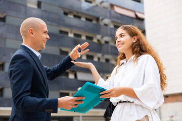 Professional builder giving keys to young woman client after finishing signing contract at...