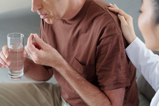 Cropped image of senior man taking pills uder control of his caregiver