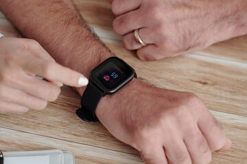 Obraz premium Close-up image of caregiver showing senior man how to check his heart rate via app on smartwatch