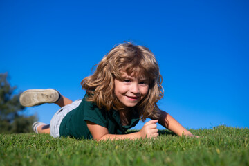 Portrait of a happy little boy laying on the grass in the park. Outdoor portrait of pretty little boy on fresh green grass. Summer fun, happy childhood.