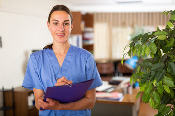 Portrait of a smiling young female doctor taking important notes of a patient's treatment while standing in the ..clinic resident's office