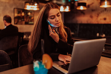 A business woman in glasses sitting in a cafe using a laptop and a smartphone for online meeting. Selective focus
