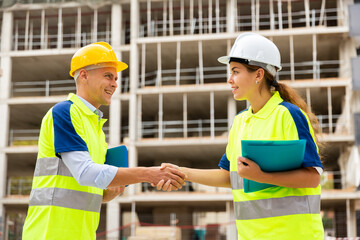 Portrait of two successful engineers on a construction site, shaking hands amicably