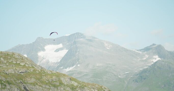Paraglider with kite flying alone above steep Loen mountain hillside - handheld
