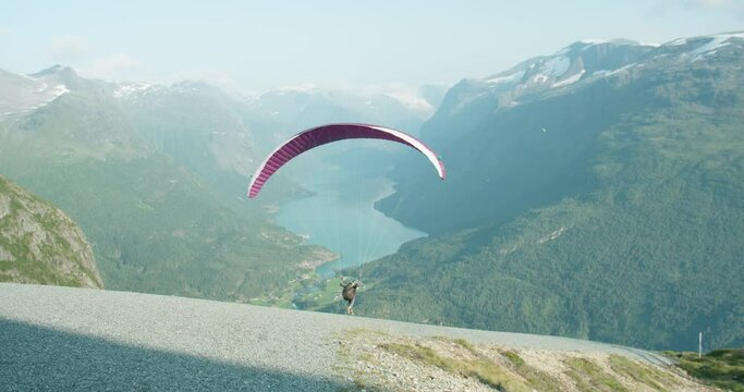 Paraglider with kite taking off from mountain with blue fjord background