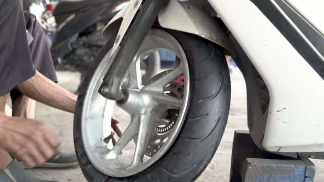 Mechanic pumping air into wheel of motorbike, static close up view