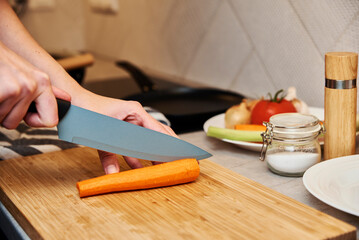 Obraz na płótnie Canvas Woman chopping carrot in kitchen, close up