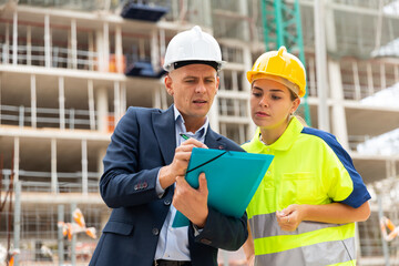 Civil engineer and a young woman worker working on a construction site discuss a construction plan, make important notes ..on tablet