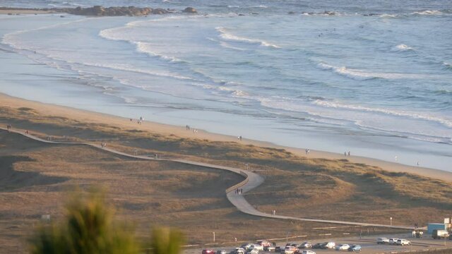 La Lanzada beach, with people walking on wooden walkway, people walking on the beach and surfers in the sea, Galicia Spain