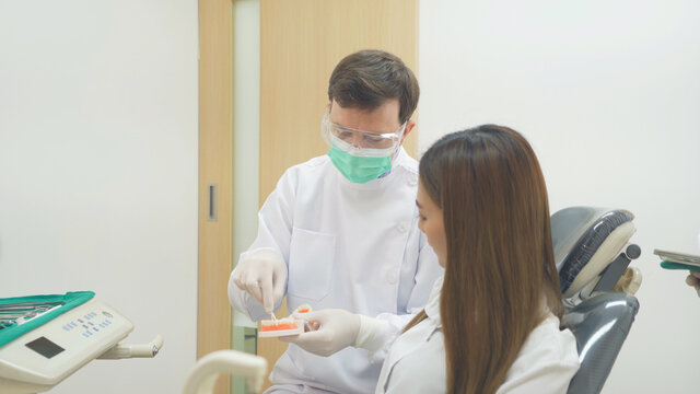 A caucasian dentist man, people showing how to use dental floss with typodont teeth model to Asian patient at hospital clinic. Cleaning. Doctor. Dentistry, medical and health.