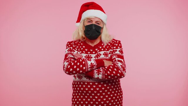 Senior grandmother woman wearing sterile face mask ppe to safe from coronavirus on lockdown quarantine. Granny indoors studio shot isolated on pink background. Covid-19 New Year Christmas celebration