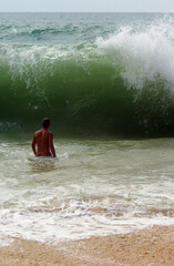 A man's figure in front of a big wave braking on a beach