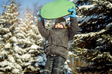 Fototapeta na wymiar cute caucasian boy holding a snow saucer to slide from hill in winter park