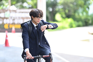 Young businessman checking time on wrist watch and riding a bicycle on the city streets. Eco Transportation and healthy active lifestyle concept.
