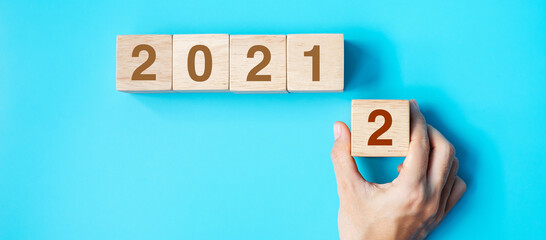 hand holding wooden cube block with 2022 text on blue background. Resolution, plan, review, goal,...