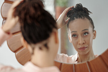 Beautiful young Black woman looking at mirror and making hair bun