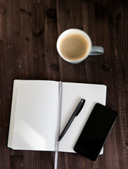 open white notebook , a black mobile phone and a cup of coffee on a dark wooden background