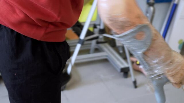 A man living with a disability with amputated legs and arms walks on modern artificial bionic legs prosthesis using old plastic arms tied to crutches with sticky tape