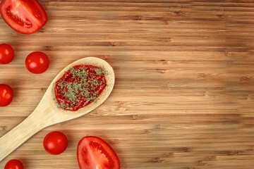 Fresh cherry tomatoes and more chopped tomatoes on a wooden background. Ketchup in a wooden spoon.