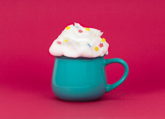 bright blue green cup with a drink decorated with whipped cream and decorative stars on a pink background close up