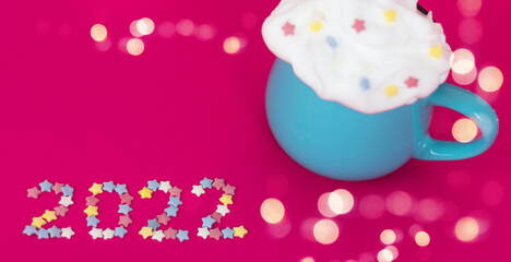number 2022 from small decorative sweet stars next to a festive drink on a bright pink background. new year concept