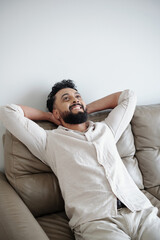 Happy man smiling and leaning back on his sofa with arms behind his head enjoying long weekend