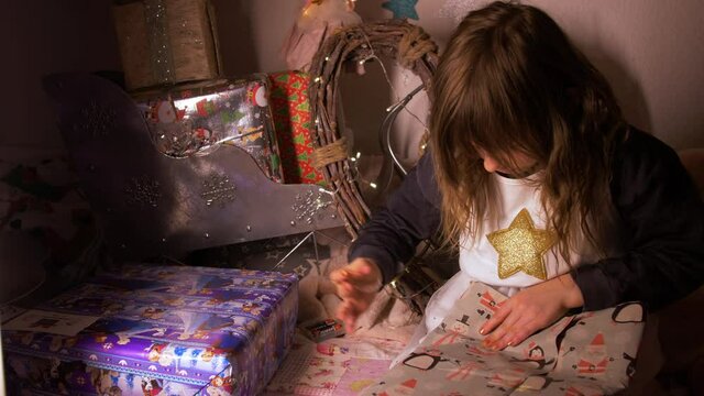 Wide Shot of little girl wrapping birthday Christmas gift at cozy home. Adorable child decorating presents with grey craft paper with penguins using tape for xmas and Santa Claus. 4K Pro Res.