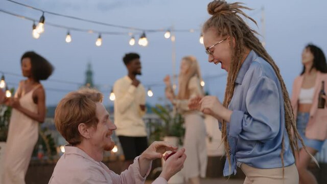 Redhead guy making proposal to woman with dreads on rooftop