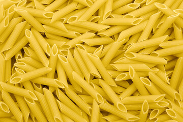 Dry uncooked penne pasta background, top view.