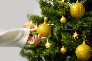Christmas tree decorating by woman with golden glitter ball and shiny ball on fir branch close up...