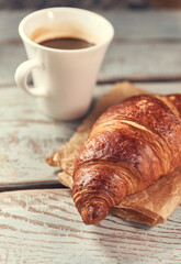Morning croissant and a cup of coffee on a wooden background