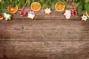 Christmas tree branches, cookies, lollipops, orange on an aged wooden table. Top view. Copy space