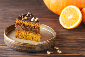 A piece of pumpkin pie with chocolate ganache, orange confit and nuts on a wooden table. Sugar, gluten and lactose free, vegan.