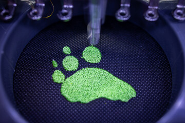 Embroidery with industrial embroidery machine - dog paw on black textiles - fill toe - motion blur...