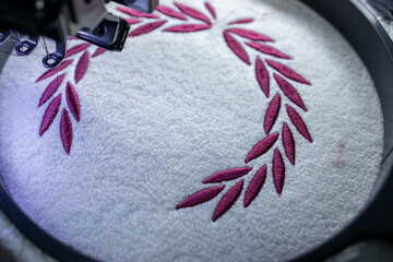 Embroidery design on white towel with burgundy thread. Embroidery by machine. Close up.
