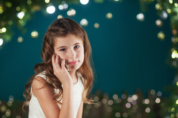 Obraz na płótnie Canvas Portrait of cute long-haired little girl in dress on background of lights. Little girl talking on phone. Christmas, New Year and birthday celebration concept. Winter holidays. Copy space