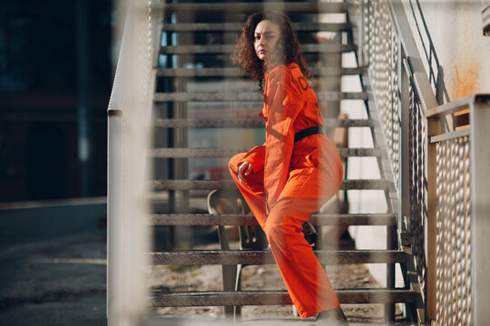 Young brunette curly woman in orange suit. Female in colorful overalls portrait