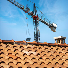 Gray and red crane and a closeup of a roof with terracotta tiles (Coppo in Italian language) on...